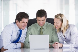 Three-businesspeople-in-office-with-laptop-smiling_ht2qd6phs
